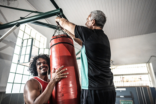 Boxers helping coach put the punching bag on boxing gym