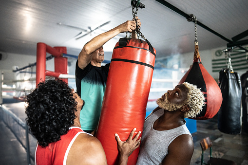 Boxers helping coach put the punching bag on boxing gym