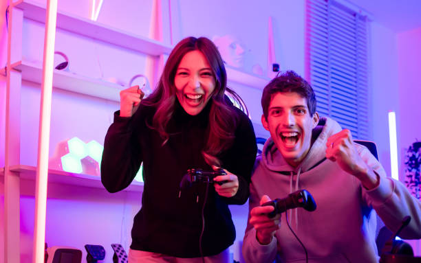 istock Couple or friends have shocking, exciting face with fun, using joystick to compete and play games together, sitting in room at home with neon decorated light. Game online streamer Concept. 1940452090