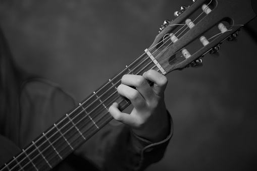 Black and white photo, studio shot, hand young guitarist playing the guitar. Classical concert, performance Close up guitar. Arts music