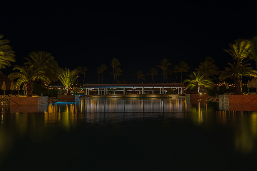 A beautiful night view of the hotel grounds with an outdoor pool and blurred palm trees reflecting in the water. Curacao.