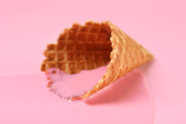 Melted ice cream and wafer cone on pink background, closeup