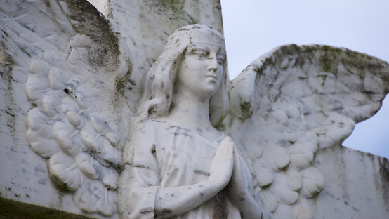 Statue of winged angel in prayer position in a cemetery