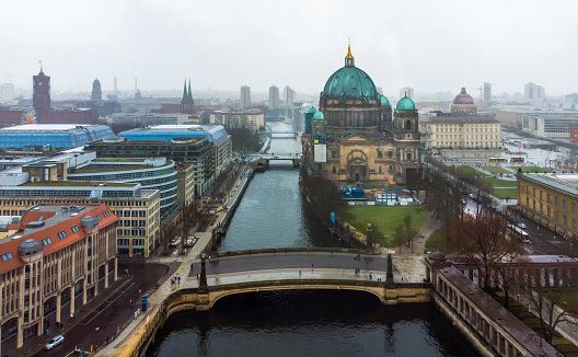 Friedrichsbrucke on Spree river. Behind -Berlin cathedral, Rotes Rathaus  - foggy day in German capital,  in Christmas eve day!    People walk at distance
with umbrellas.   Lustgarten in right corner
