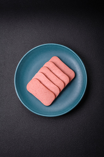 Delicious canned pink ham with salt, spices and herbs on a dark concrete background