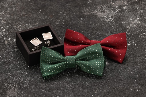 Stylish color bow ties and box of cufflinks on grey textured background