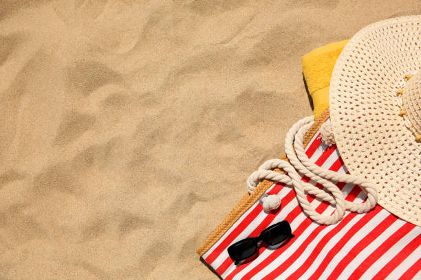 istock Striped beach bag, sunglasses, towel and hat on sand, flat lay. Space for text 1940627524