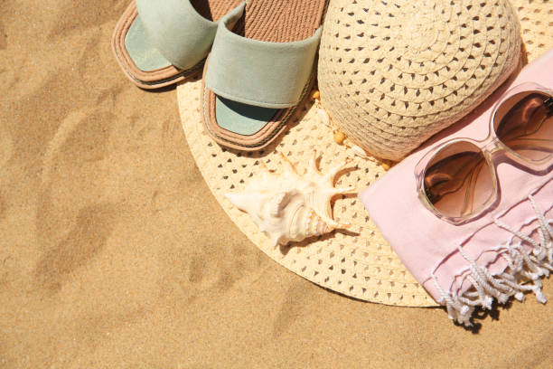 istock Straw hat, sunglasses, towel and slippers on sand, above view. Space for text 1940628038