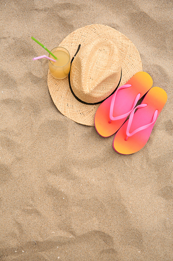 Straw hat, flip flops and refreshing drink on sand, flat lay with space for text. Beach accessories