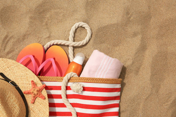 istock Stylish striped bag with beach accessories on sand, flat lay. Space for text 1940629079
