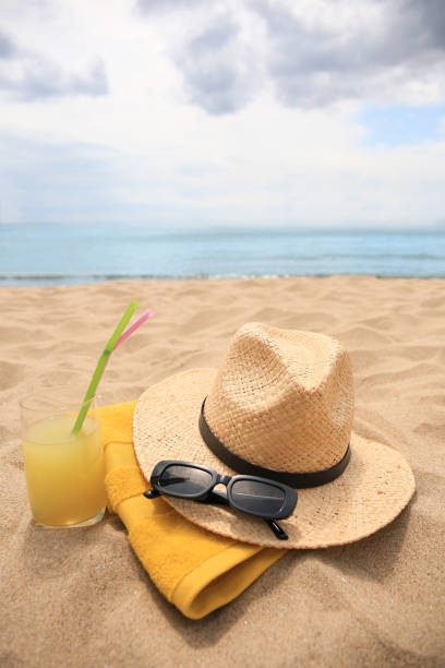istock Straw hat, sunglasses, towel and refreshing drink on sandy beach near sea. Space for text 1940629089