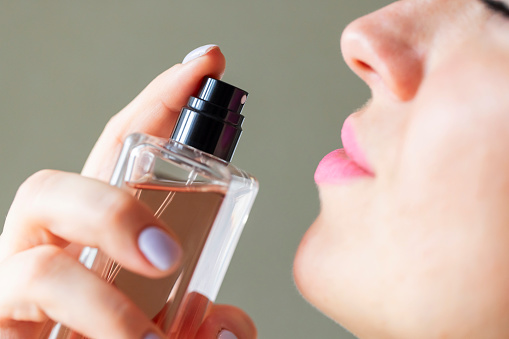 Close-up image of a woman with pink lipstick spraying fragrance from a glass perfume bottle, highlighting the sense of smell.