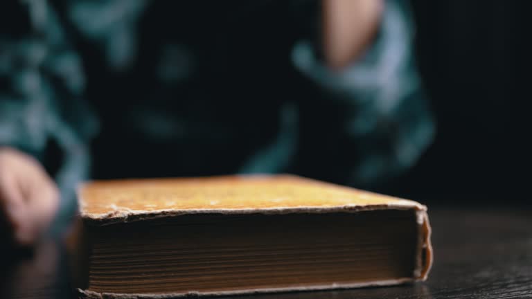 Close up, a Woman Hands Flipping through the Page of an Old Book in a Dark Room