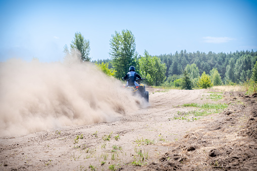 Rear view of dirt bike race riding fast on off-road dirt track.