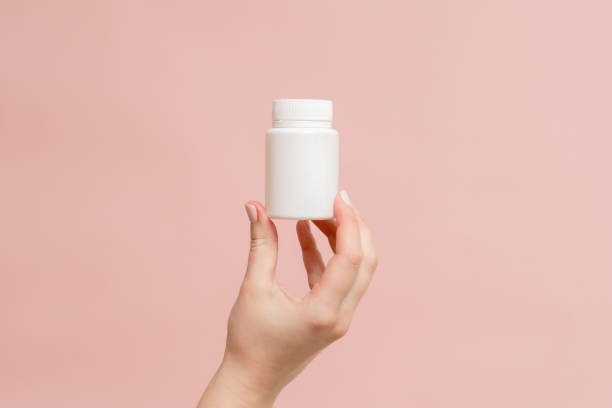 istock White bottle (plastic tube) in hand on pink background. Packaging for vitamins, pill or capsule, or supplement. Mockup for product branding 1940650534