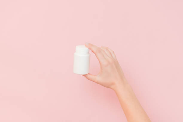 istock View on white bottle plastic tube in hands on pink background. Packaging for pills, capsules, supplements or ointment. Cosmetics 1940657417