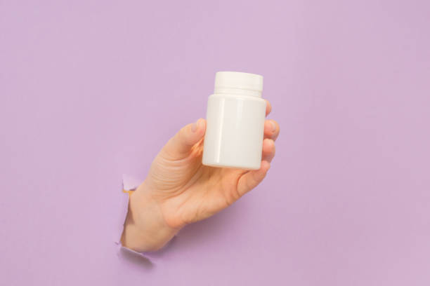 istock View on white bottle plastic tube in hands on lilac background. Packaging for pills, capsules, supplements. Cosmetics 1940657952