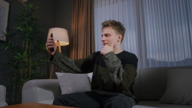 istock Handsome blonde man sitting on sofa having video call conversation with smart phone. Share news, talk to family, enjoy webchat virtual meeting 1940666817