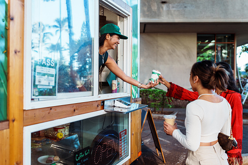 Smiling barista hands coffee to customer