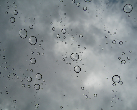 Raindrops on a window with clouds in the background.