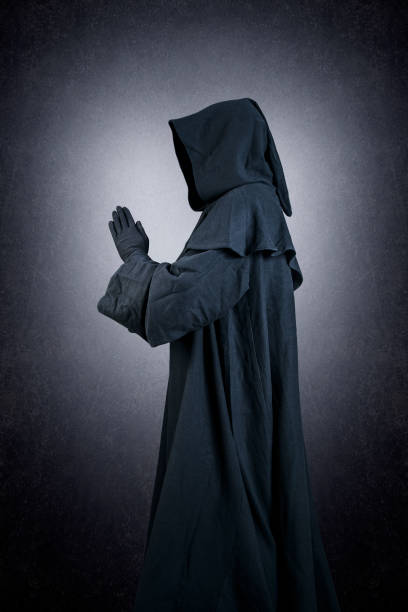 istock Medieval monk in hooded cloak praying in the dark 1940675201