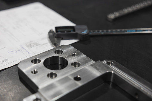 Detailed view of a modern machining workspace, showcasing precision engineered metal pieces, plans and a caliper.