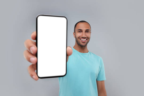 istock Young man showing smartphone in hand on light grey background 1940697452