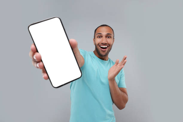 istock Surprised man showing smartphone in hand on light grey background 1940697802