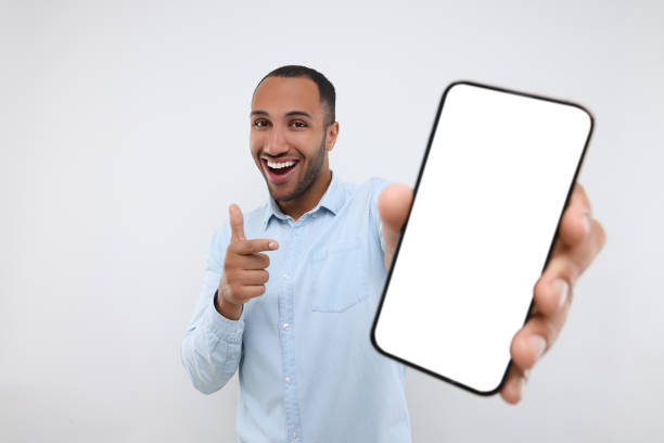 istock Young man showing smartphone in hand and pointing at it on white background 1940697969