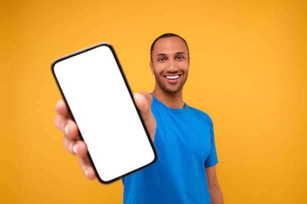 istock Young man showing smartphone in hand on yellow background 1940697974