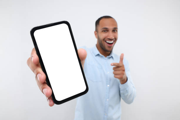 istock Young man showing smartphone in hand and pointing at it on white background, selective focus. Mockup for design 1940701094
