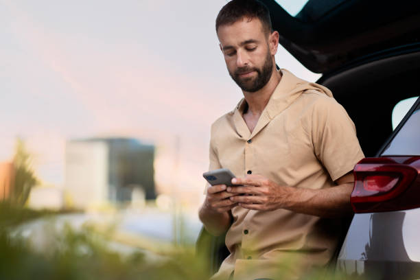 istock Latin man using mobile phone reading text message, checking email, communication online near car 1940716604