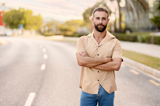 Portrait of handsome bearded latin man with arms crossed looking at camera standing on the road, copy space