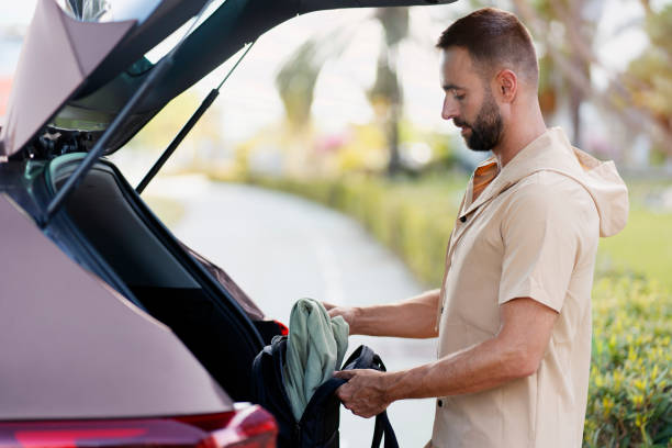 Bearded man loading bag in car trunk, transportation concept