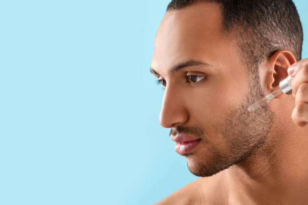 istock Handsome man applying cosmetic serum onto face on light blue background, closeup. Space for text 1940739257