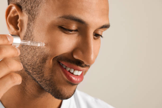 istock Handsome man applying cosmetic serum onto face on light grey background, closeup. Space for text 1940745521