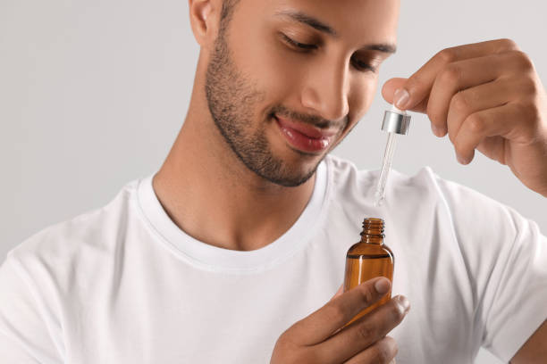 istock Handsome man with cosmetic serum in hands on light grey background 1940746040