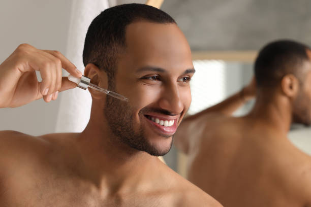 istock Handsome man applying cosmetic serum onto face in bathroom, space for text 1940746546