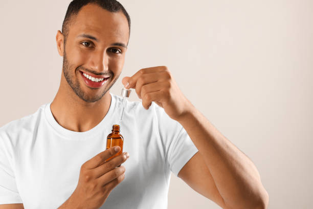 istock Handsome man with cosmetic serum in hands on light grey background, space for text 1940746555