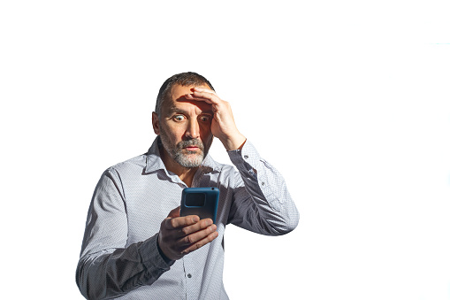Madrid, Spain. Half-length view of a mature, bearded man, incredulous and surprised, while looking at his mobile phone. White background.