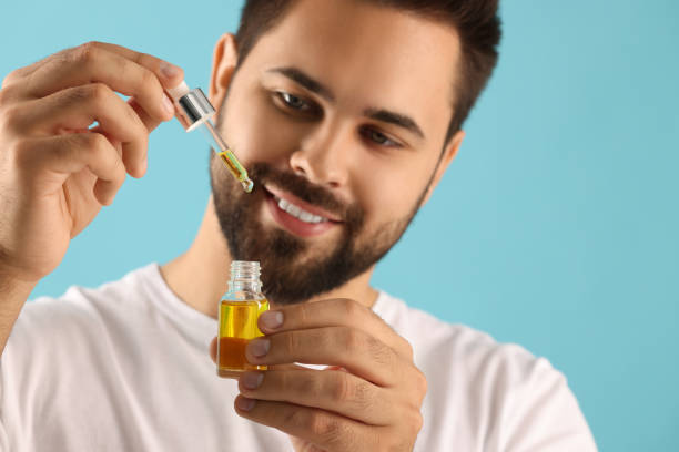 istock Handsome man with cosmetic serum in hands on light blue background, selective focus 1940765958