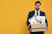 Unemployed man with box of personal office belongings on orange background. Space for text