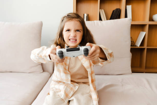 istock Angry little girl holding game console playing video games while sitting on comfortable sofa 1940780117
