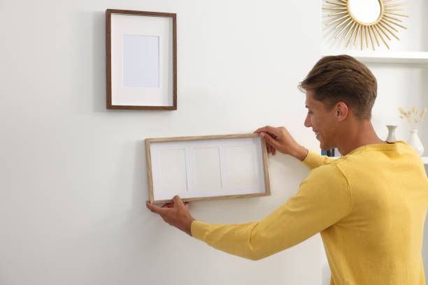 istock Young man hanging picture frames on white wall indoors 1940790509