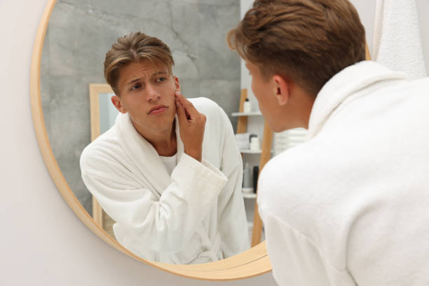 istock Upset young man looking at mirror and touching pimple on his face indoors. Acne problem 1940790539