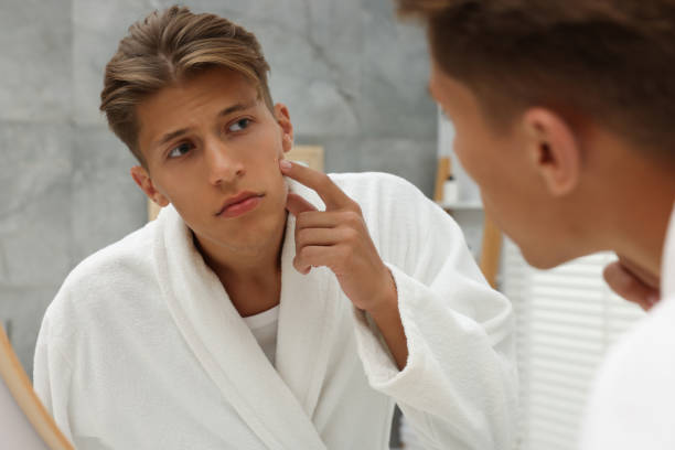 istock Upset young man looking at mirror and touching pimple on his face indoors. Acne problem 1940791058