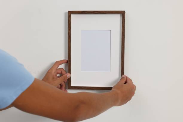 istock Young man hanging picture frame on white wall indoors, closeup 1940791584