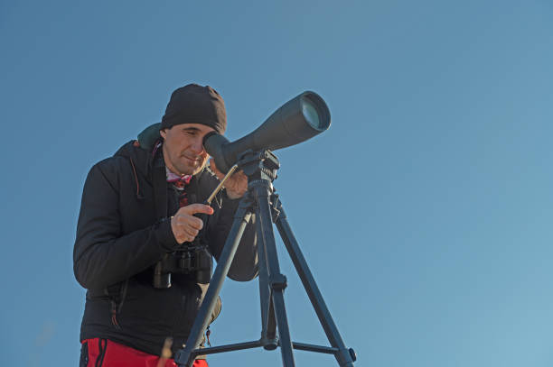 birdwatcher, wildlife photographer with telephoto lens hiding in high dry grassland outdoors on cloudy day waiting to take pictures