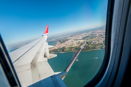 Lisboa, Portugal - July 20 2016: Looking out of a Norwegian airplane window while in the air. Passing the 25th April Bridge in Lisbon.