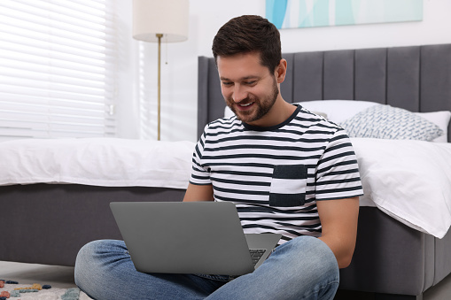 Happy man having video chat via laptop in bedroom